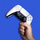 A hand grips the PlayStation 5 controller by its right handle in front of a blue background.